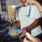 Person serving pasta into a blue bowl in a kitchen setting